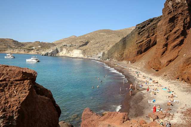 An aerial view of people on the sand next to cliffs at Red Beach, Santorini, Greece