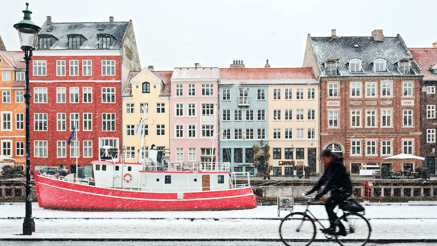 Cyclist on Copenhagen Canal with colourful buildings and red boat