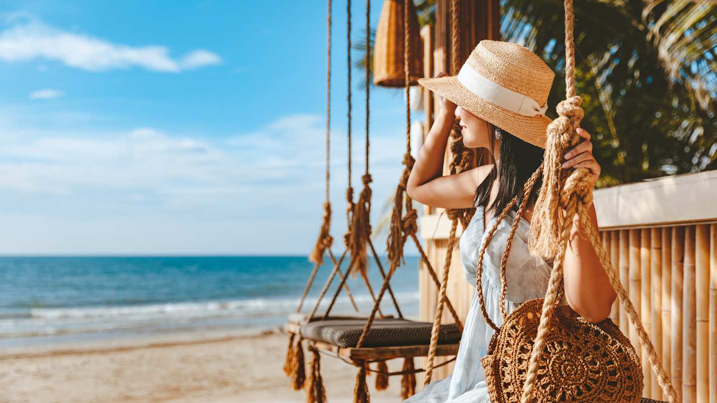 A woman sitting on a relaxing swing at the beach in a hot destination