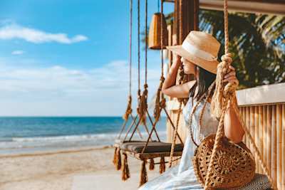 A woman sitting on a relaxing swing at the beach in a hot destination