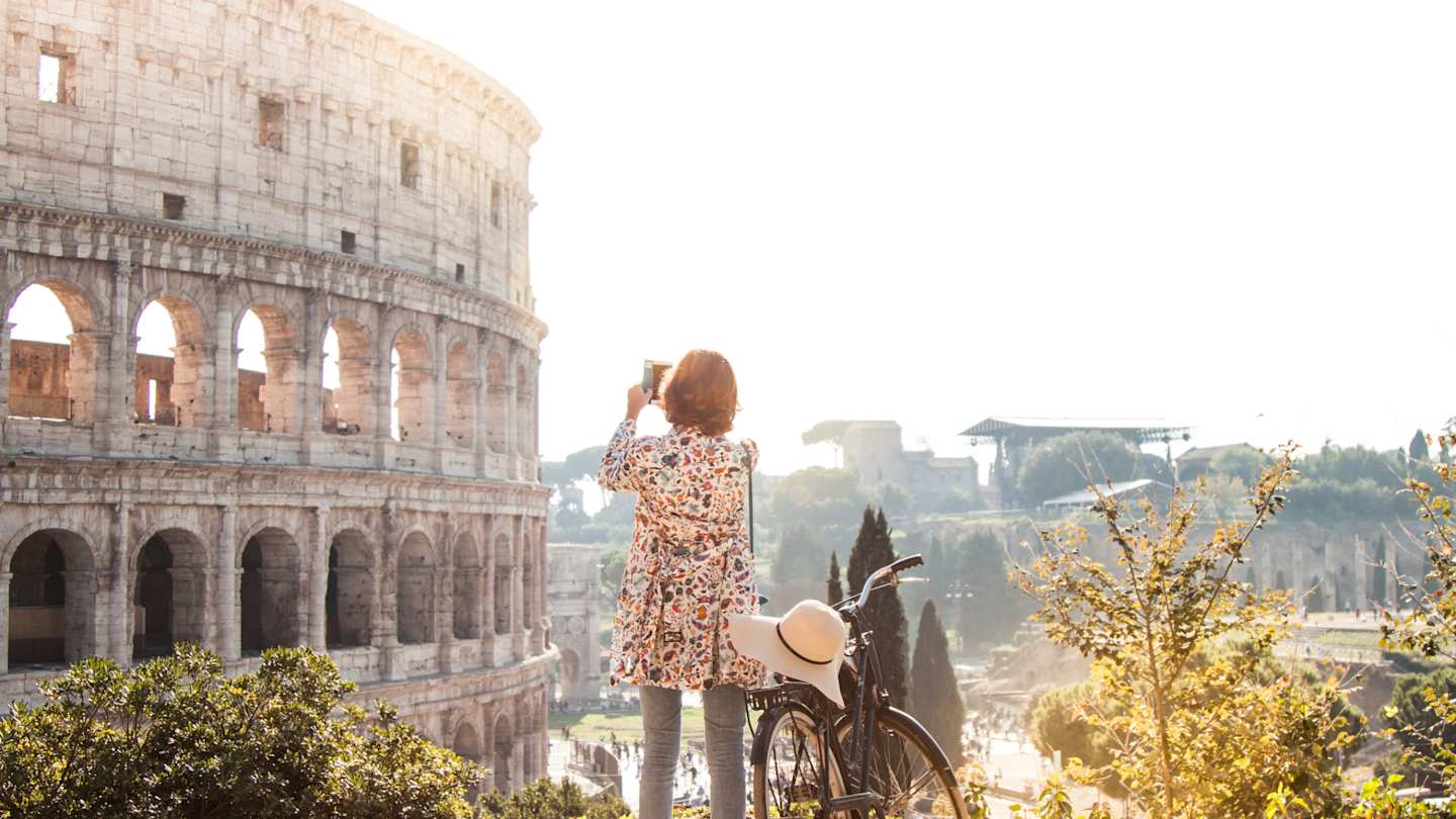 A woman with a bicycle taking a picture of the Colosseum on a solo travel trip, Rome, Italy