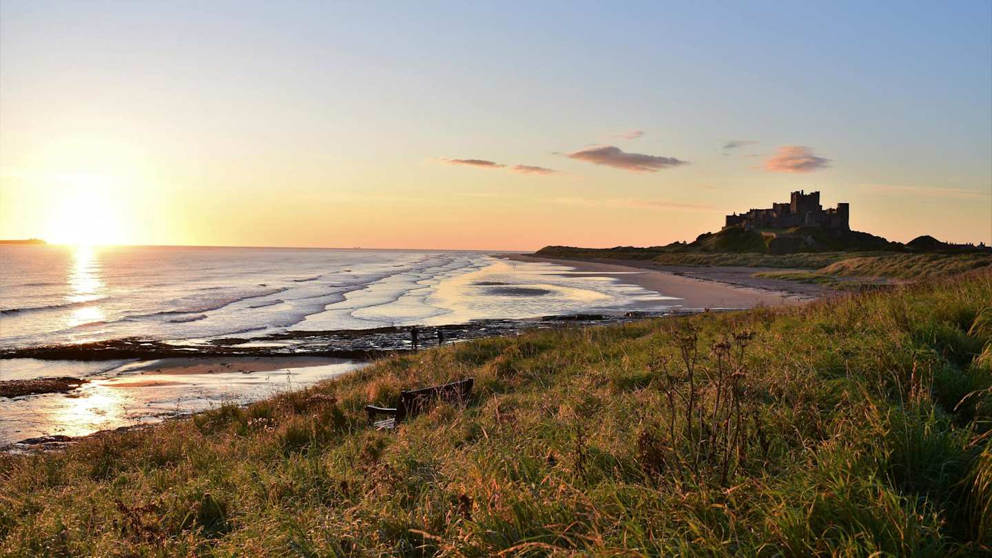 A wide-angle shot of the beach in Bamburgh, with the castle in the distance at sunset, Northumberland, England, UK