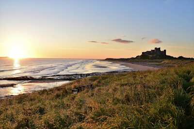 A wide-angle shot of the beach in Bamburgh, with the castle in the distance at sunset, Northumberland, England, UK