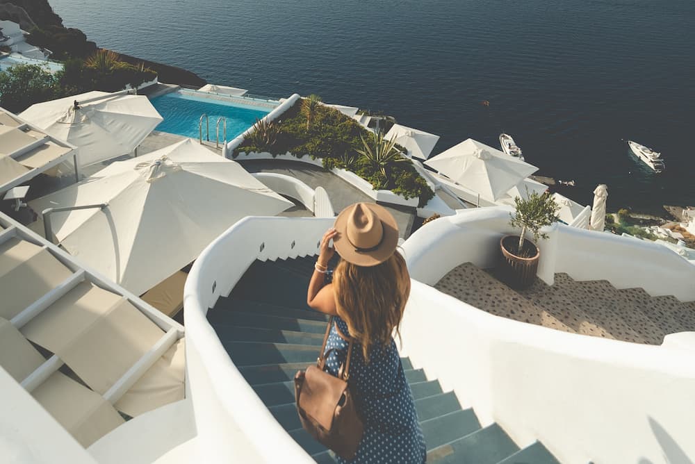 Woman wearing a blue dress and brown hat walking down stairs while looking out to the sea.