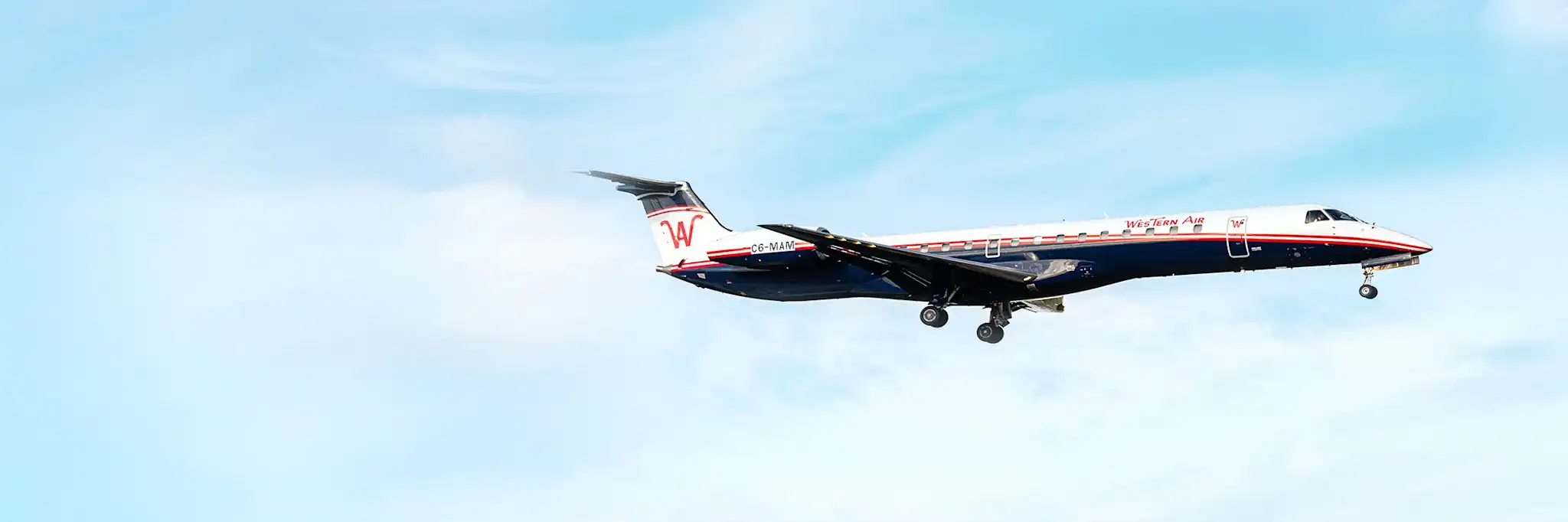 A Western Air Embraer ERJ 145 regional jet, registration C6MAN, descending for landing with its gear down against a bright, partly cloudy blue sky.