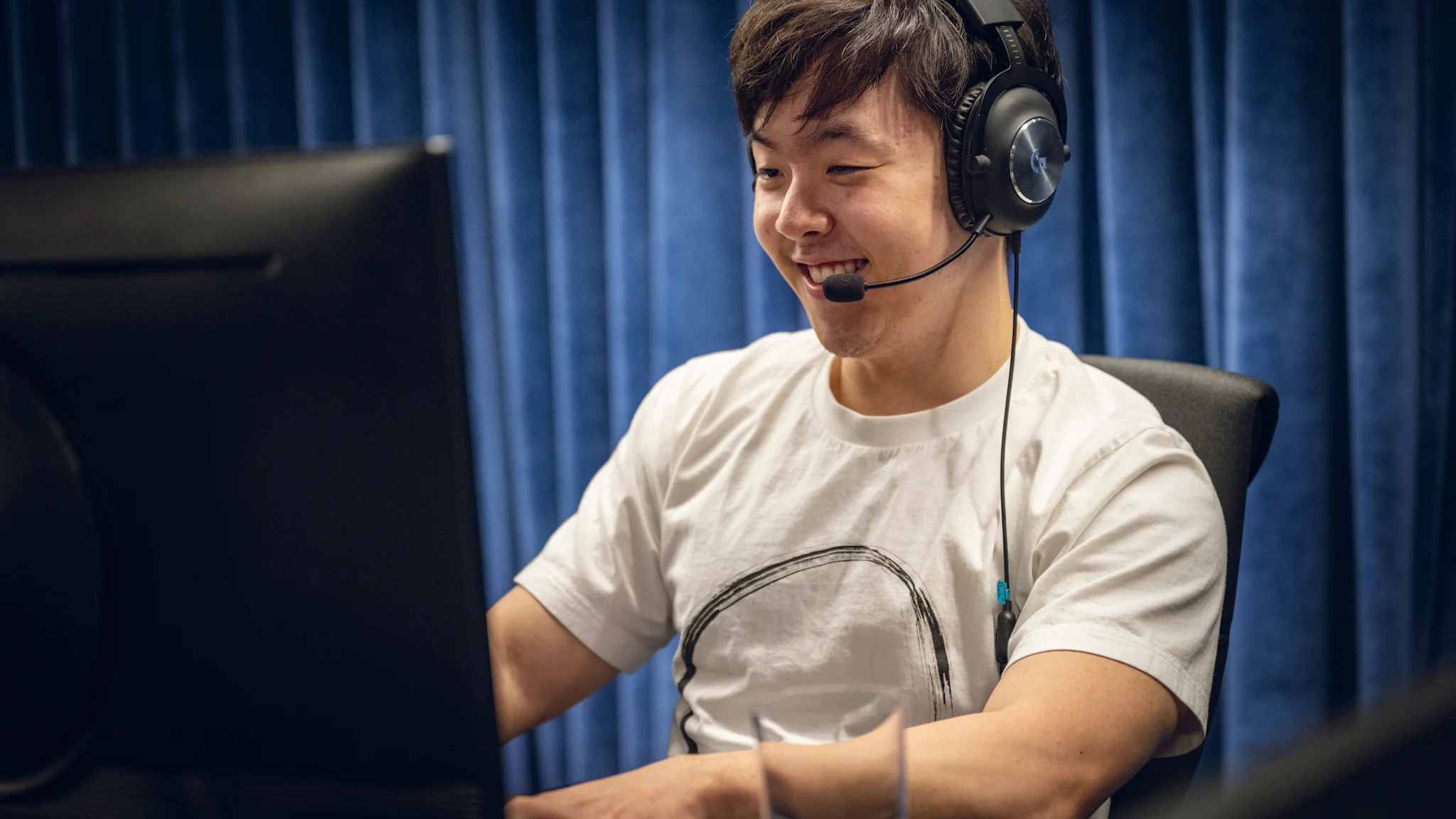 A male gamers sits in front of a computer testing March of Giants smiling wearing a headset