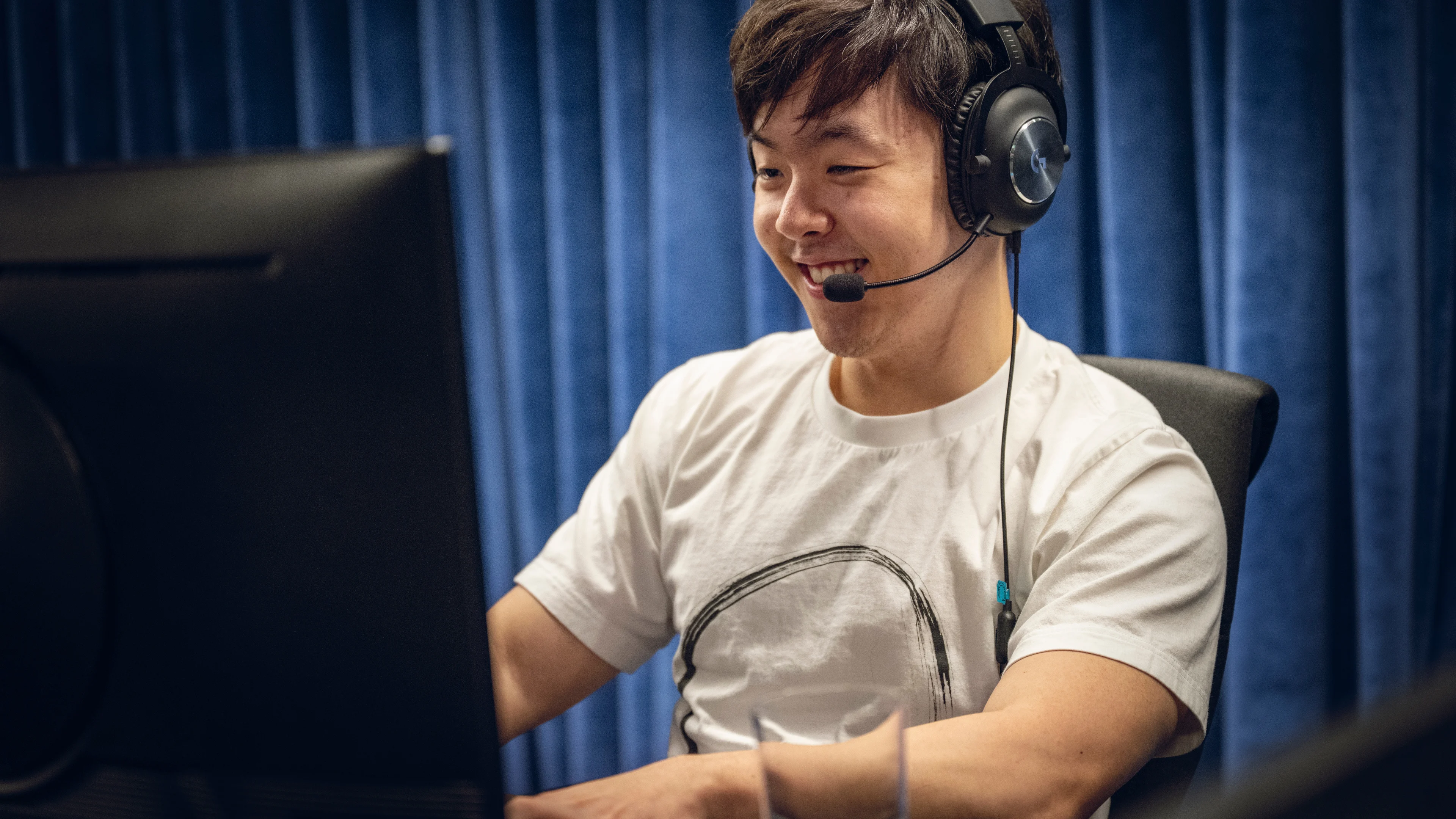 A male gamers sits in front of a computer testing March of Giants smiling wearing a headset