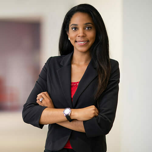 BIPOC professional woman smiling with her arms crossed in a black blazer and red blouse