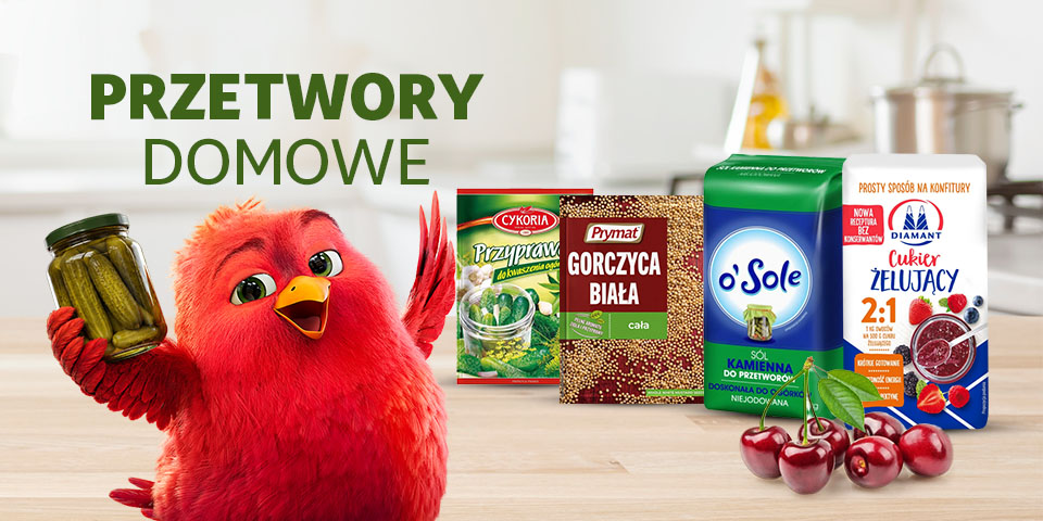 Baner reklamowy z czerwonym, puchatym ptakiem trzymającym słoik ogórków. Obok niego produkty do przetworów: przyprawa, gorczyca, sól i cukier żelujący. W tle rozmyta kuchnia, na pierwszym planie wiśnie. Napis: "PRZETWORY DOMOWE".