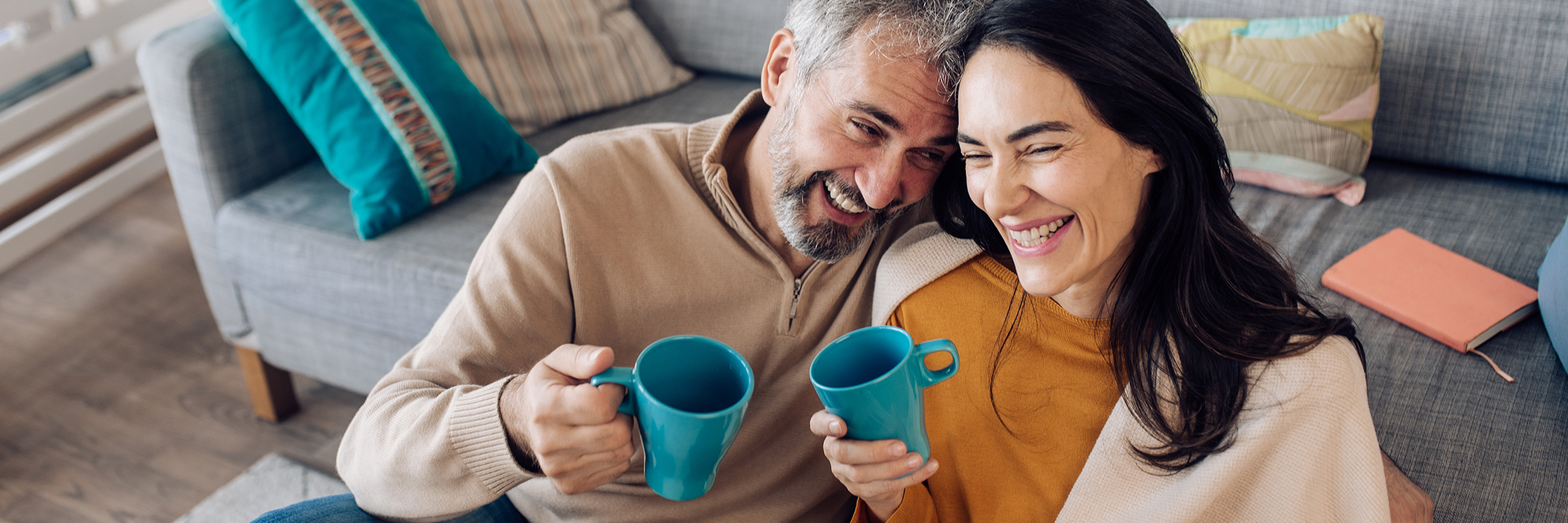 Couple in their home smiling and drinking coffee.