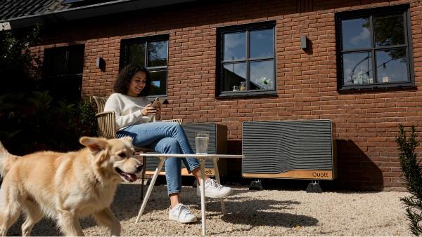 Quatt 14kw monoblock buitenunit tegen gevel geplaatst vrouw zit er voor op haar telefoon en golden retriever hond rent