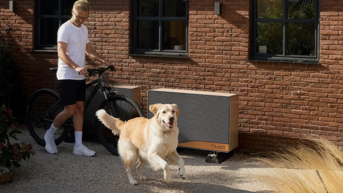 Quatt 14kw monoblock buitenunit tegen gevel geplaatst man loopt er langs met fiets en golden retriever hond rent