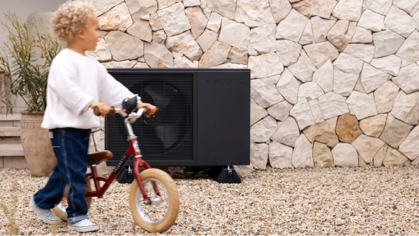 WeHeat Flint monoblock buitenunit tegen gevel aan kind loopt er met fietsje langs