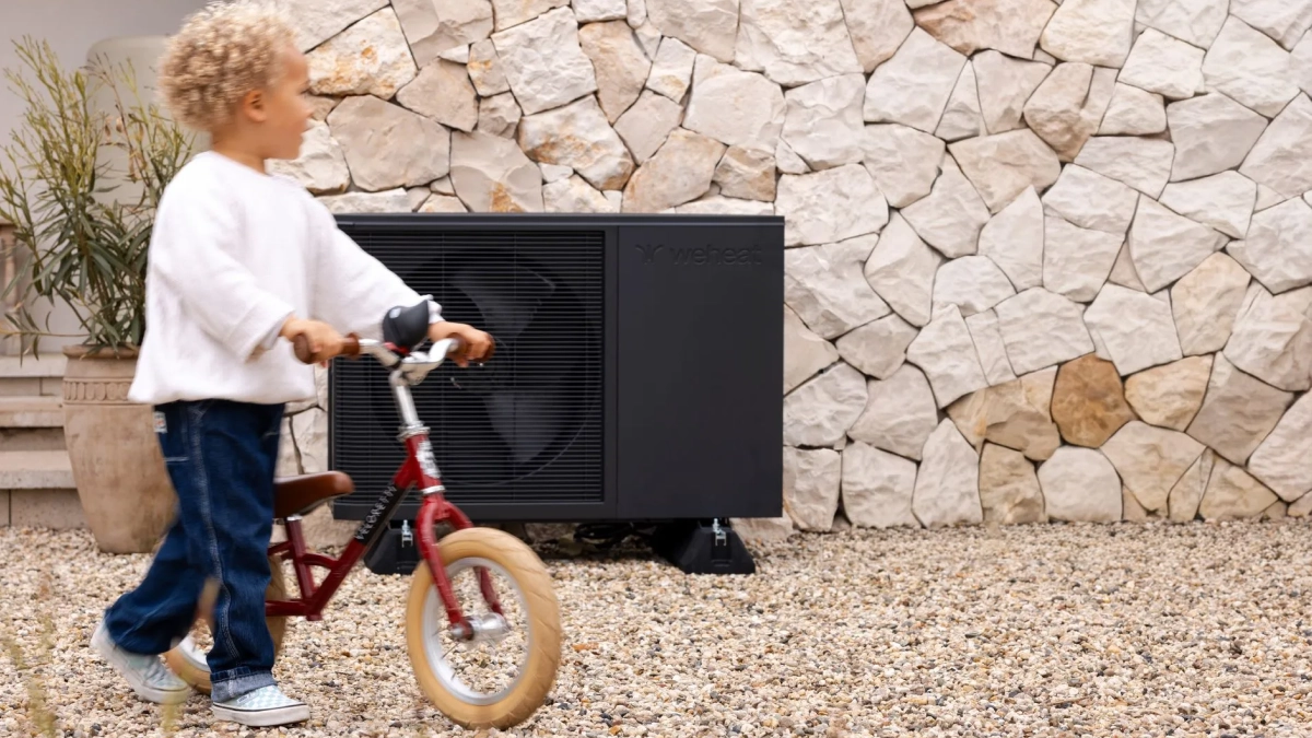 WeHeat Flint monoblock buitenunit tegen gevel aan kind loopt er met fietsje langs