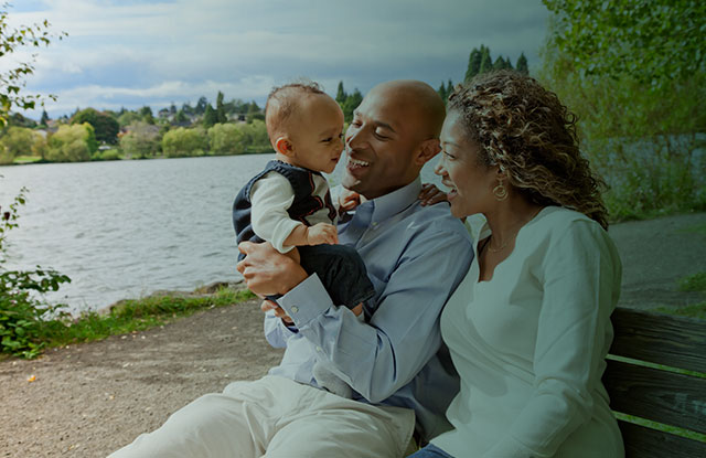 Man with a baby in his arms, and a woman sitting on a bench