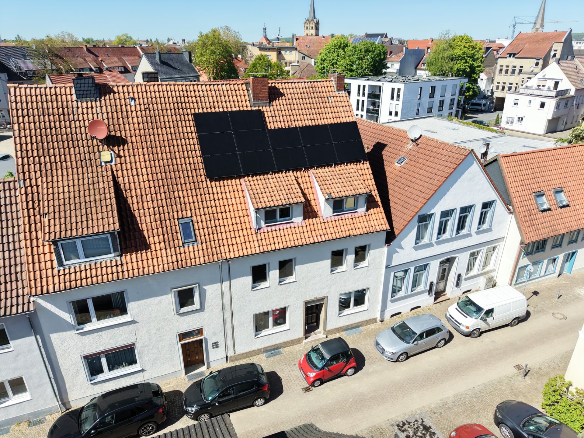 Reihenhäuser mit rotem Ziegeldach und Solarpanelen, geparkte Autos davor.