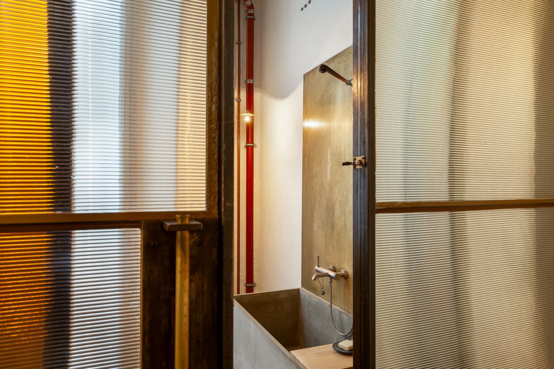 Waschbecken mit Wasserhahn hinter einer geriffelten Glastür, rohes Wanddesign sichtbar.