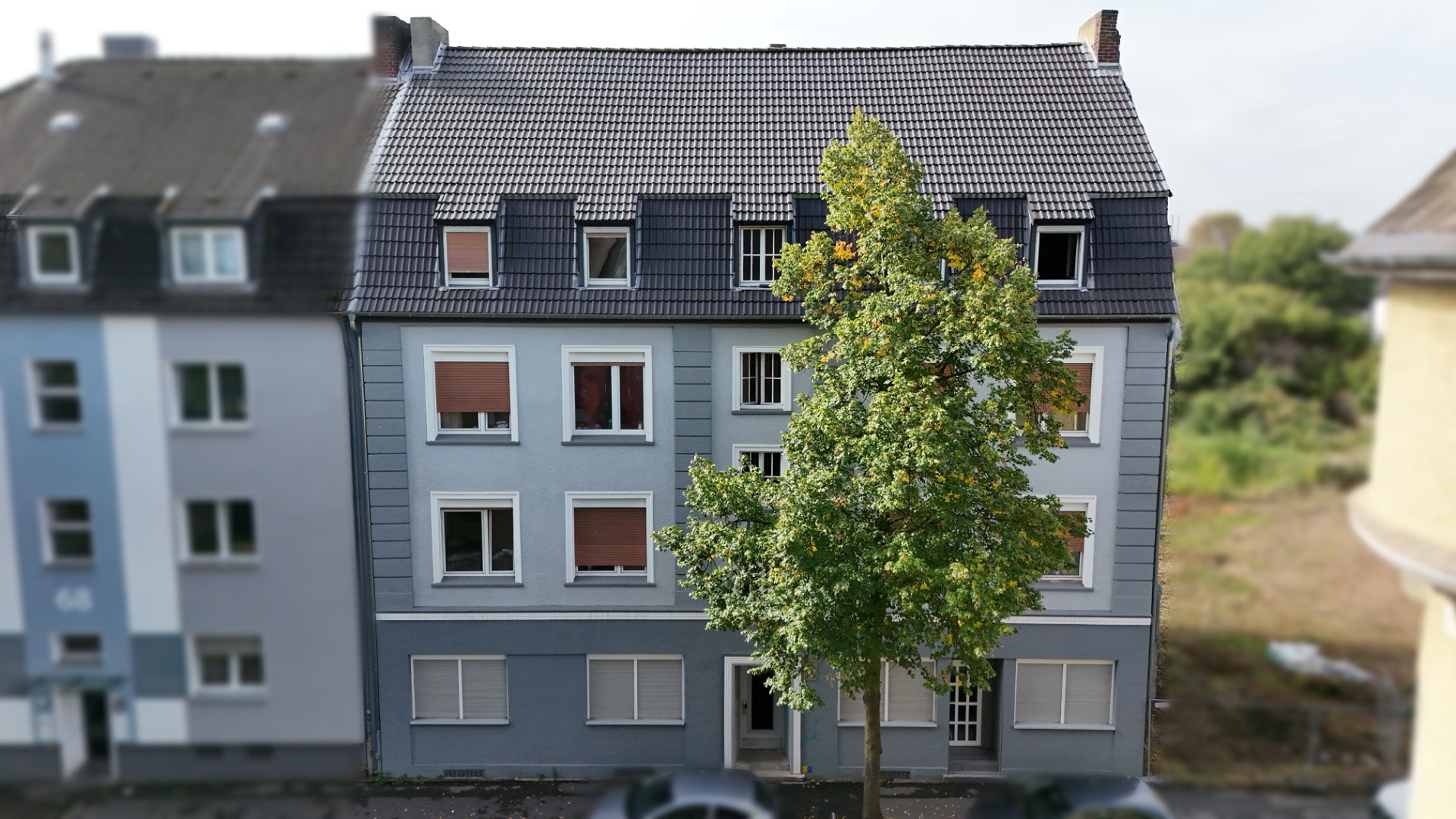 Mehrstöckiges Wohnhaus mit grauer Fassade und einem großen Baum davor.