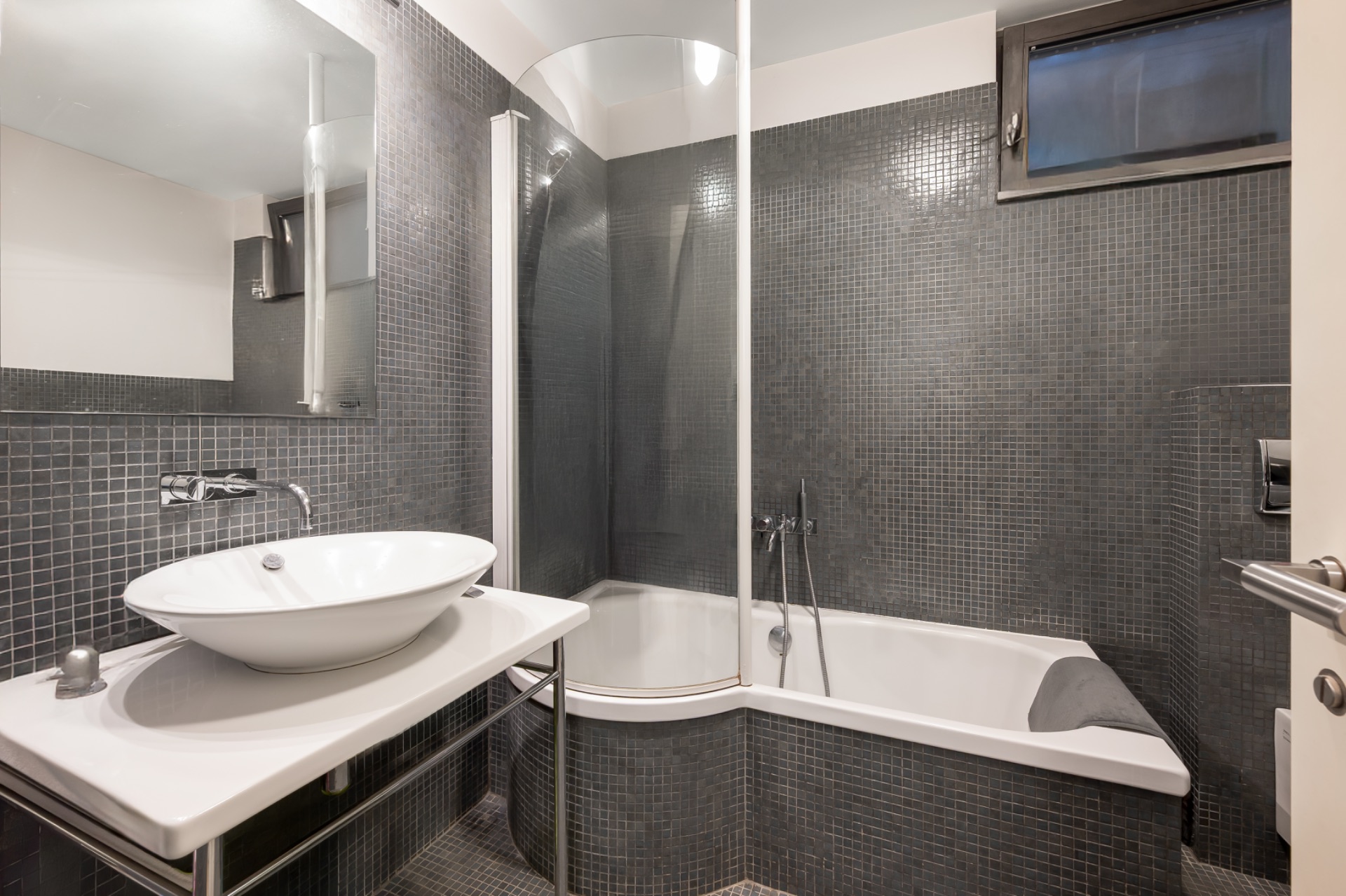 Modernes Badezimmer mit Waschbecken, Spiegel, Badewanne und grauen Fliesen.