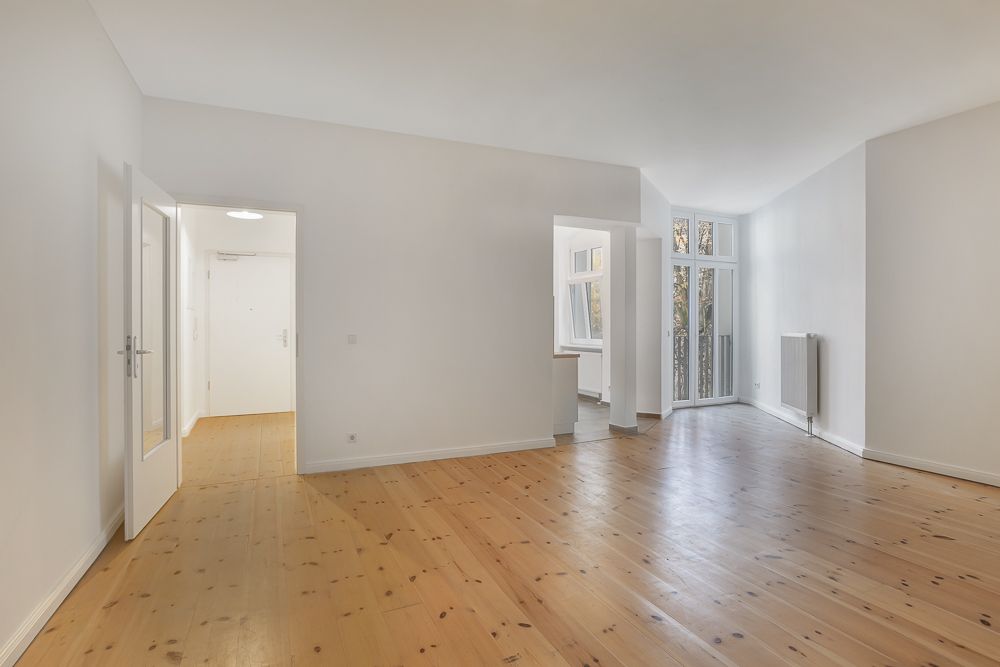 Heller, leerer Wohnraum mit Holzboden, weißen Wänden und großen Fenstern.
