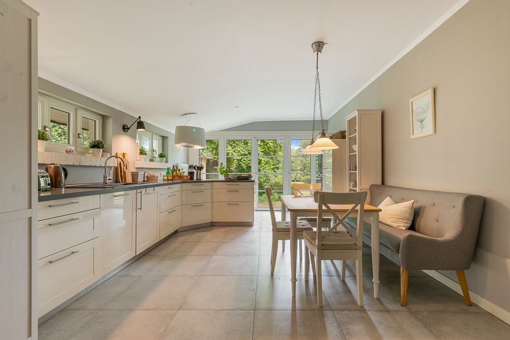 Helle Wohnküche mit Esstisch, Sofa, großen Fenstern und modernen Einbauten.