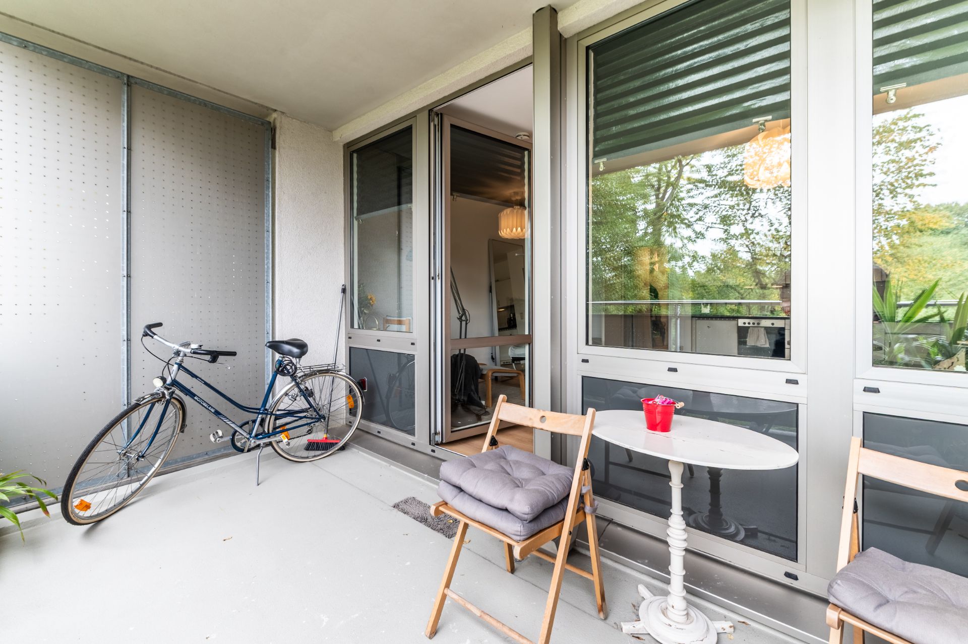 Balkon mit zwei Stühlen, einem kleinen Tisch, einem Fahrrad und Blick ins Wohnzimmer.