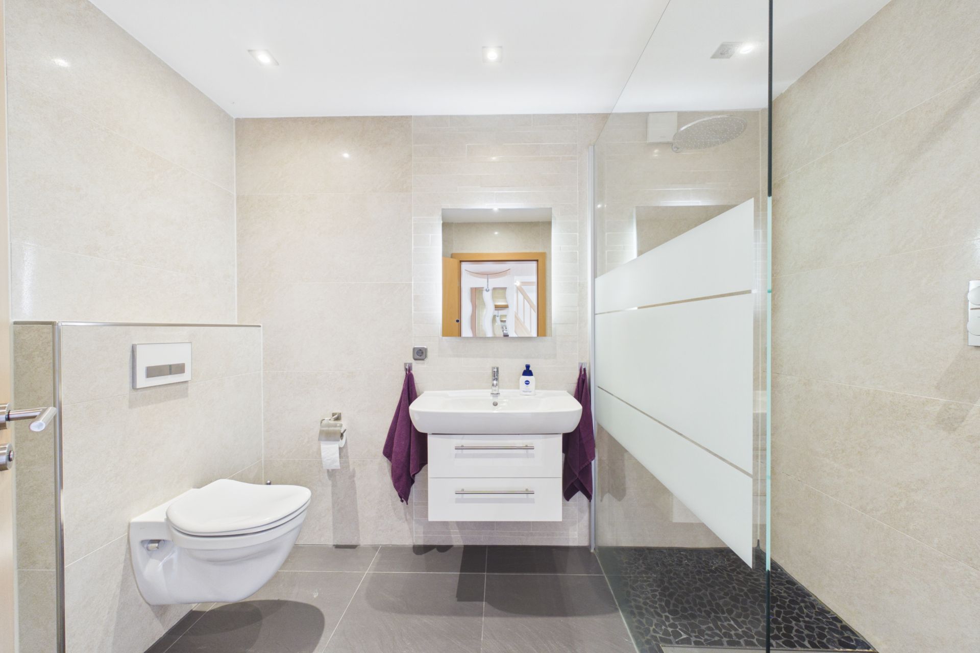 Modernes Badezimmer mit WC, Waschbecken, Spiegel und Glasdusche.