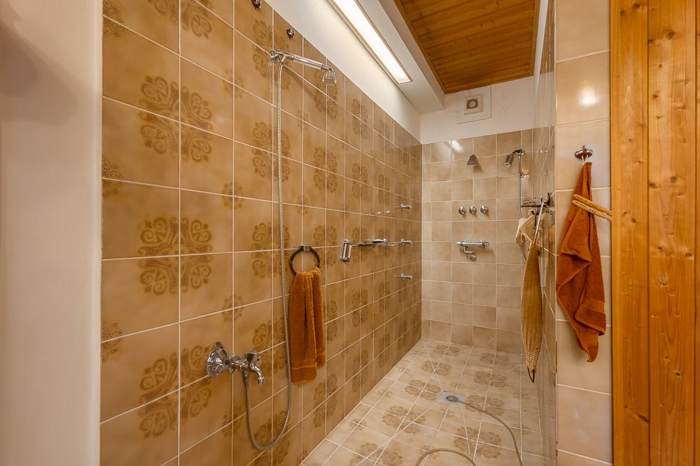 Geflieste begehbare Dusche mit mehreren Duschköpfen und braunen Handtüchern an den Wänden.