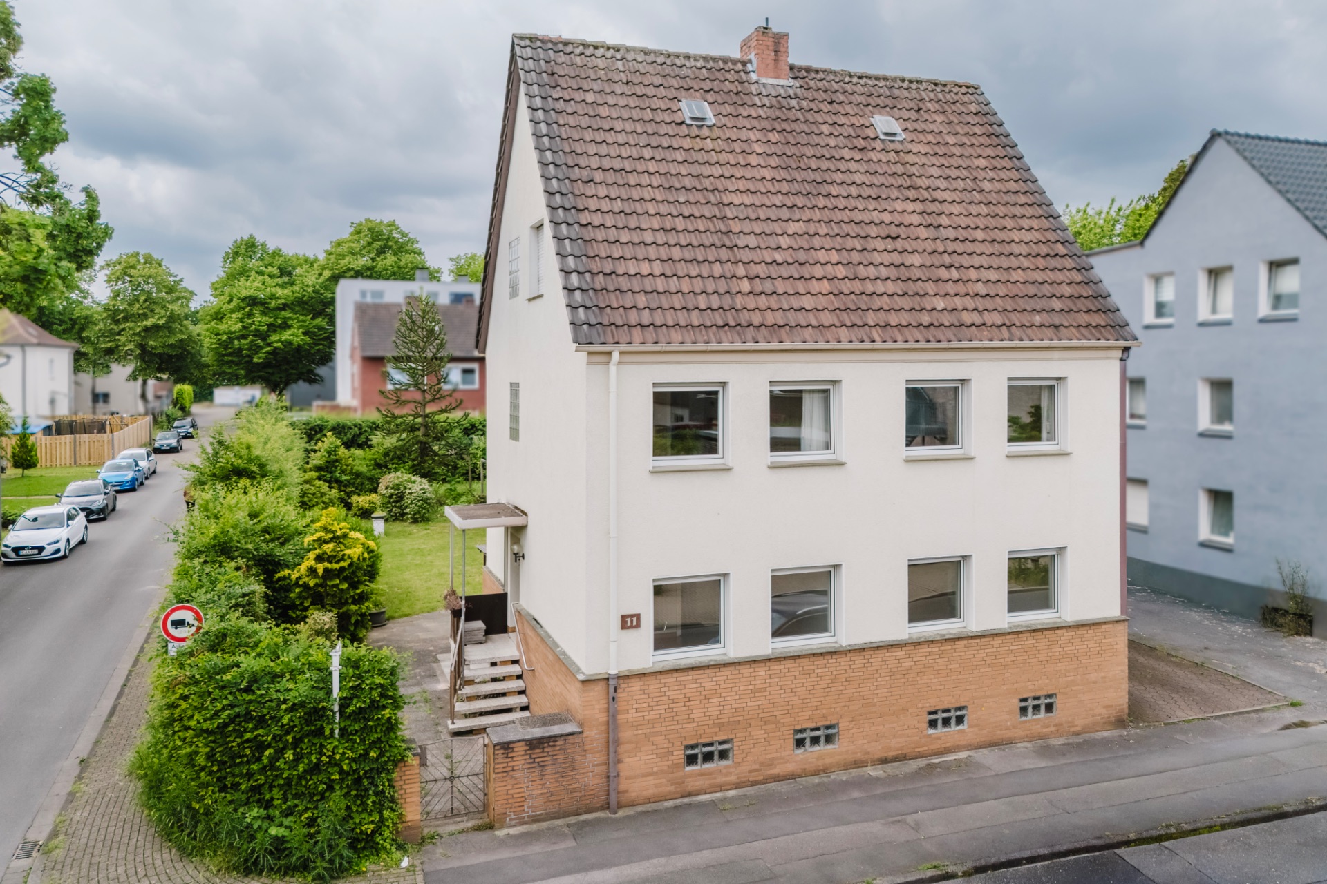 Zweistöckiges Wohnhaus mit Satteldach und Vorgarten an einer Straßenecke.
