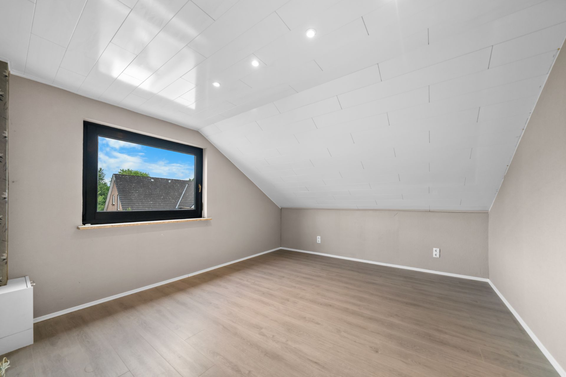 Heller Dachraum mit schräger Decke, großem Fenster und Holzfußboden.