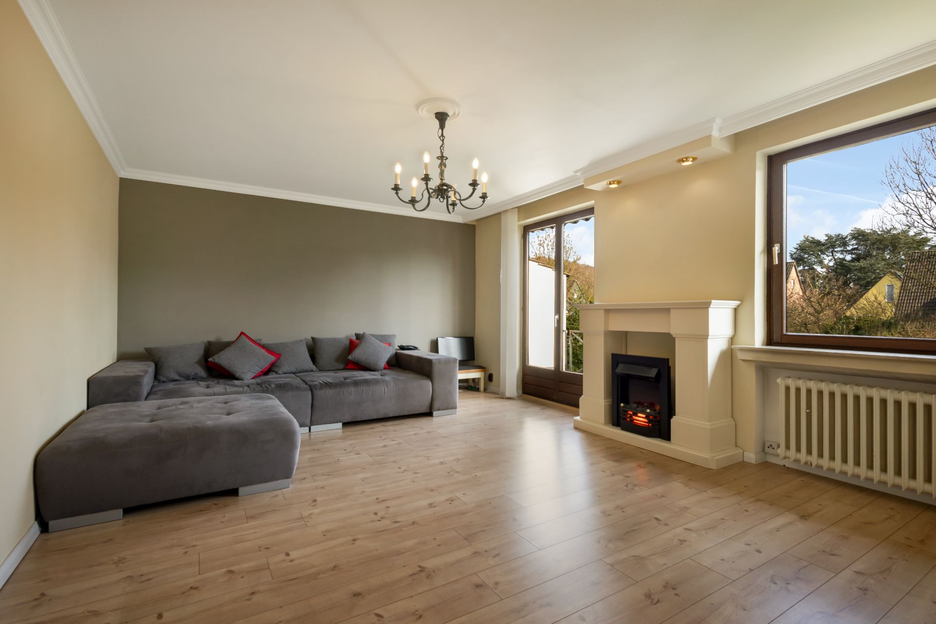Helles Wohnzimmer mit grauem Sofa, Kamin, großem Fenster und Holzboden.