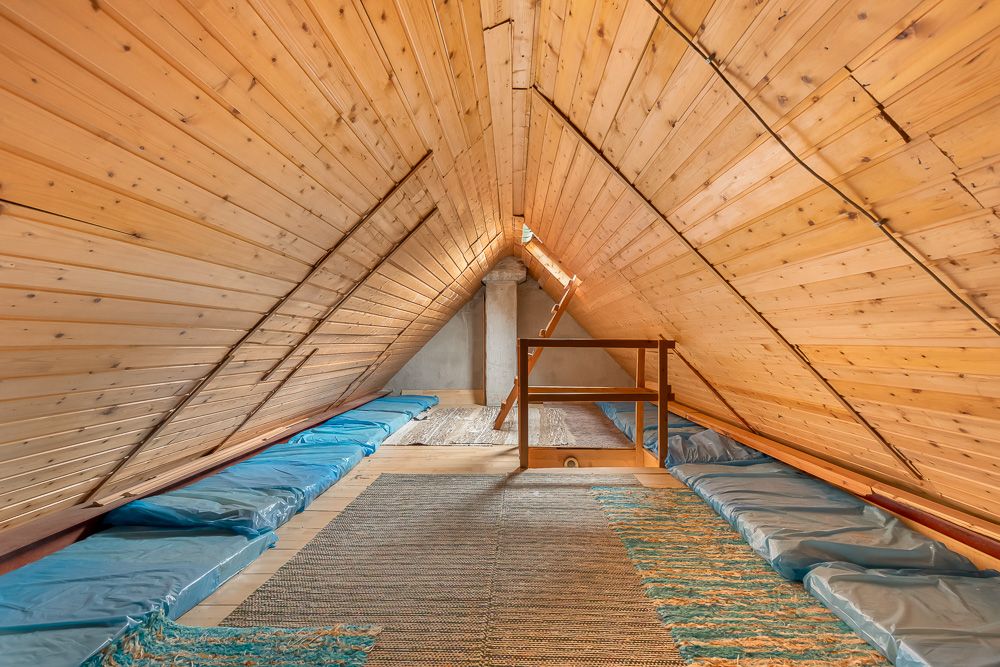 Dachbodenraum mit Holzverkleidung, Matratzen am Boden und sichtbarer Treppe.