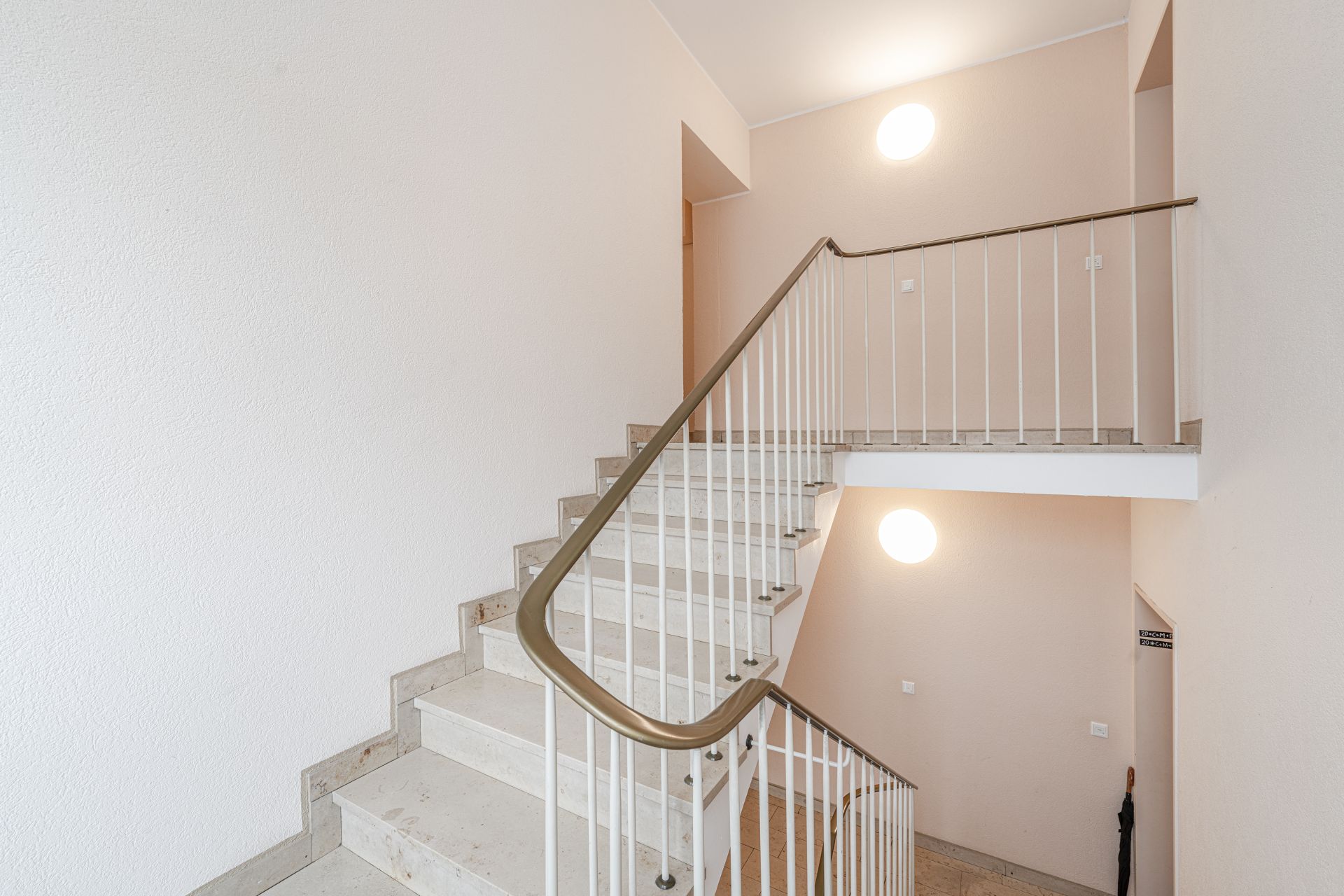 Helles Treppenhaus mit beigen Wänden, Handlauf und runden Wandlampen.