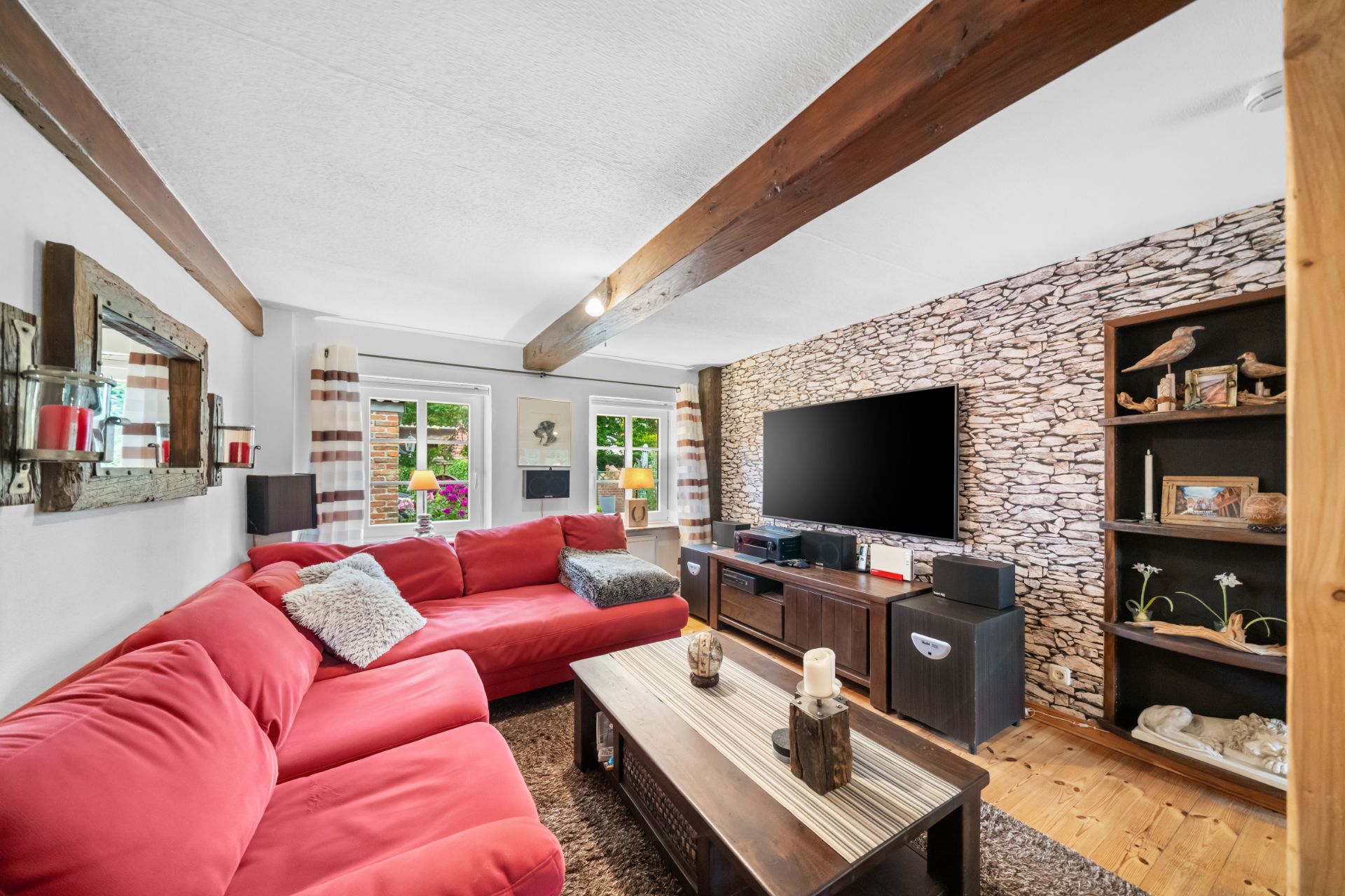 Wohnzimmer mit rotem Sofa, großem Fernseher, Holzmöbeln und Steinwand.