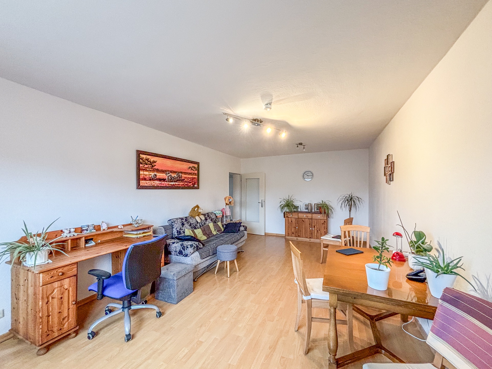 Helles Wohnzimmer mit Schreibtisch, Sofa, Esstisch und mehreren Zimmerpflanzen.
