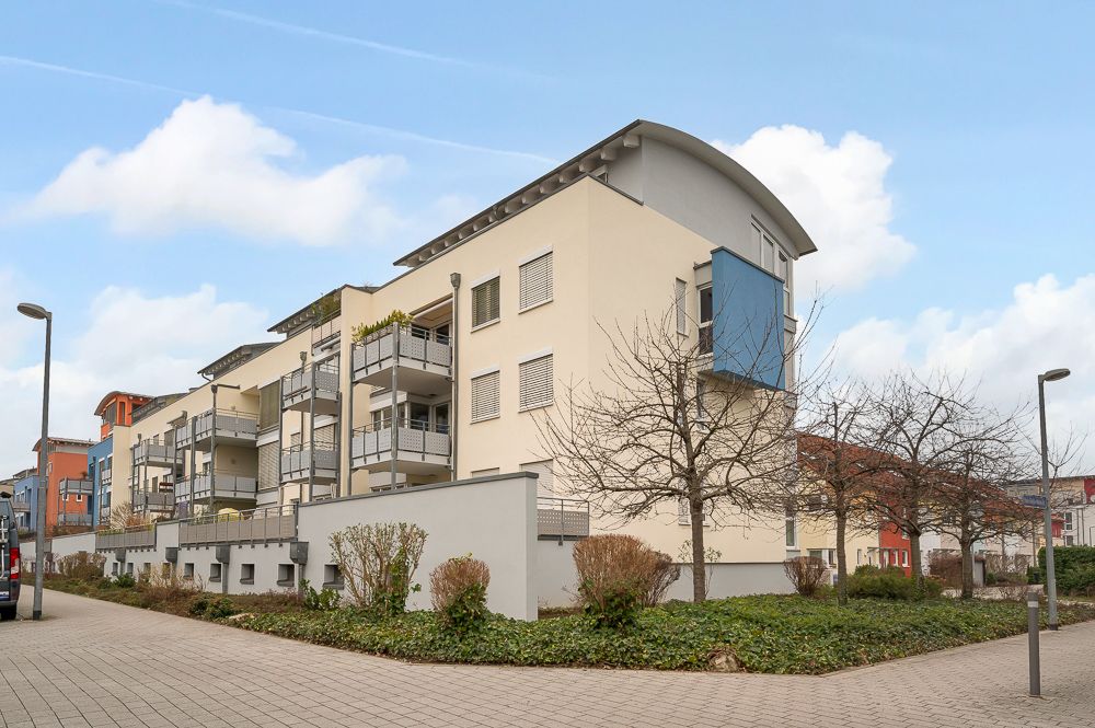 Mehrfamilienhaus mit Balkonen, mehreren Etagen und bepflanztem Vorgarten an einer ruhigen Straße.