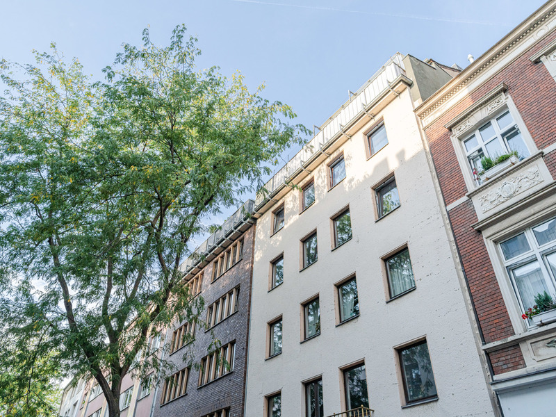 Mehrstöckiges Wohnhaus mit vielen Fenstern und Baum davor bei Tageslicht.