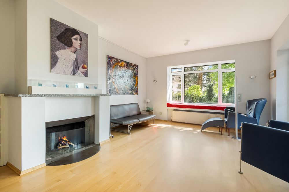 Helles Wohnzimmer mit Kamin, modernen Möbeln, großem Fenster und Gemälden an den Wänden.