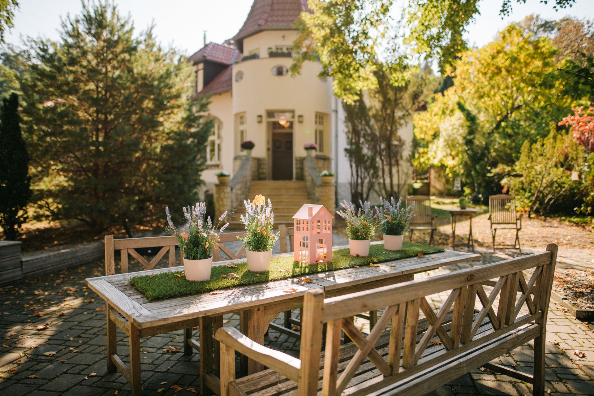 Holztisch mit Bänken und Blumendekoration im Garten vor einem Wohnhaus.