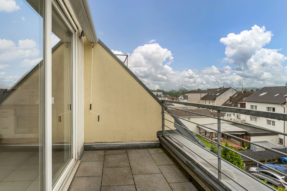Balkon mit Fliesenboden, Geländer und Blick auf Nachbarhäuser unter blauem Himmel.