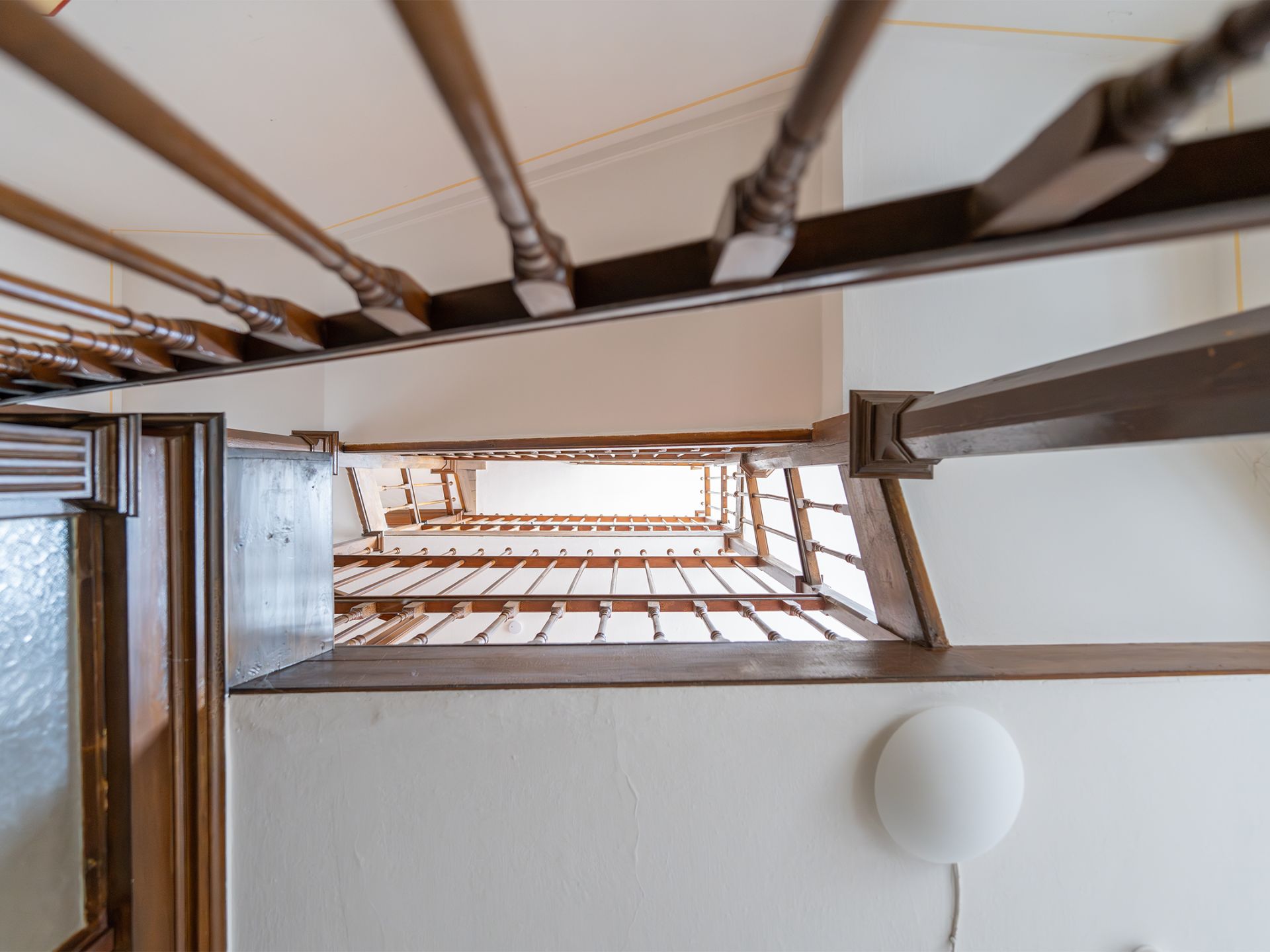 Blick von unten durch ein Treppenhaus mit Holzgeländer in einem Wohnhaus.