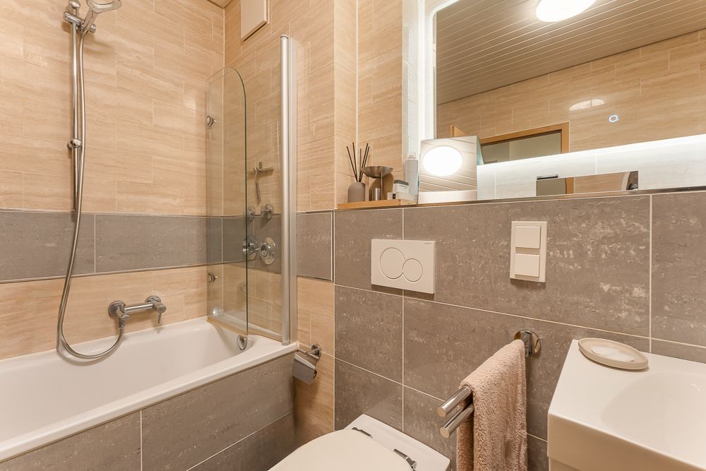 Modernes Badezimmer mit Badewanne, Dusche, Toilette, Handtuch und großem Spiegel.