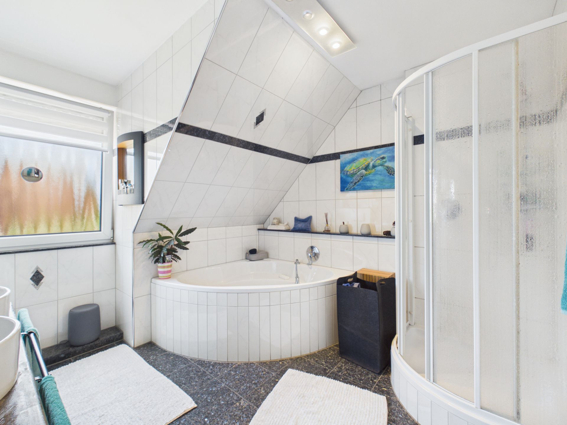 Helles Badezimmer mit Eckbadewanne, Runddusche, Fenster und schräger Decke.