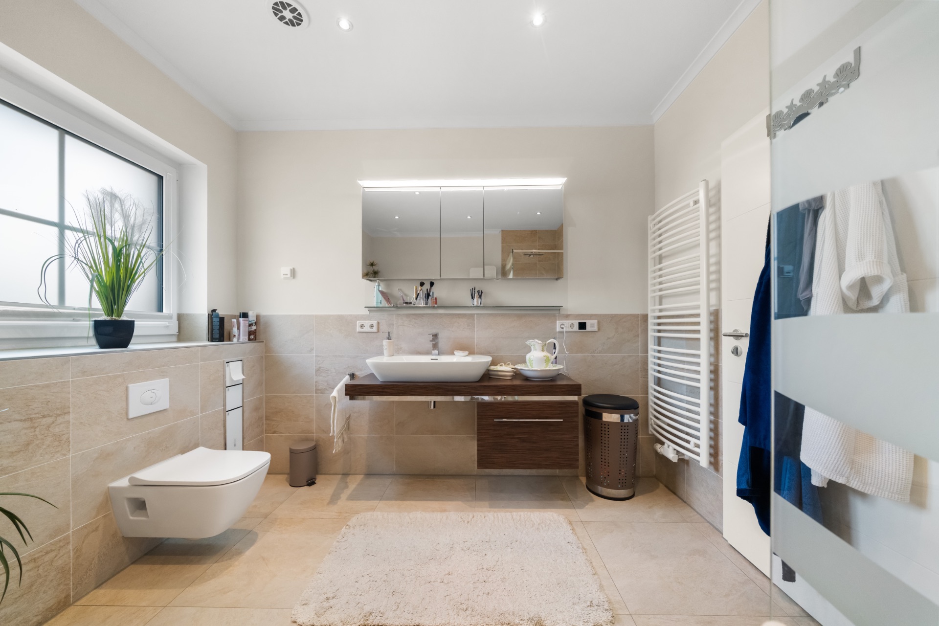 Modernes Badezimmer mit Wandtoilette, Waschbecken, Spiegel, Heizung und Fenster.