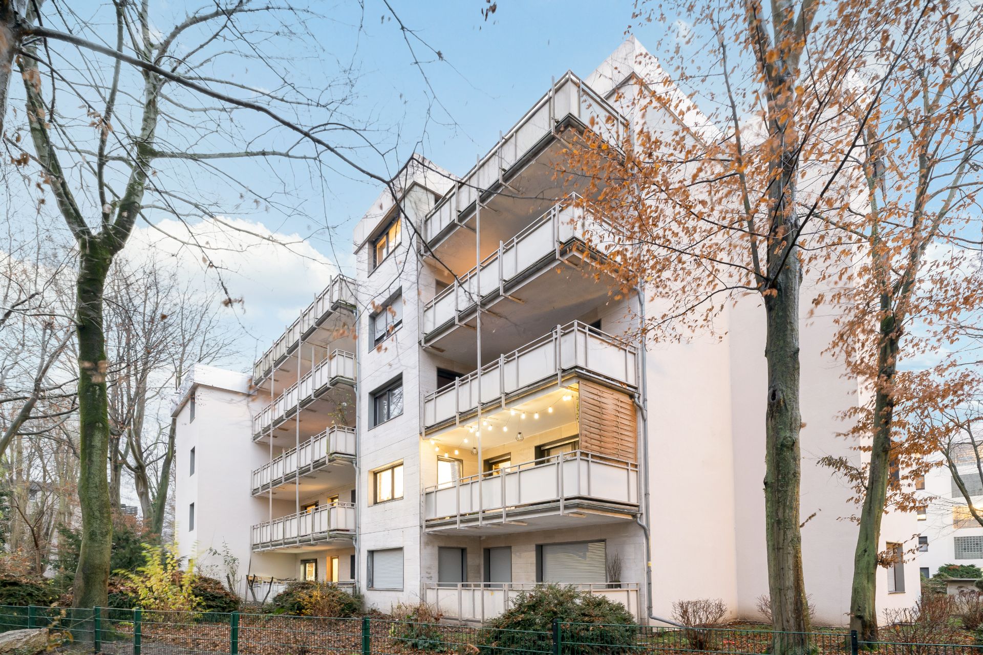 Mehrstöckiges Wohnhaus mit mehreren Balkonen, umgeben von Bäumen im Herbst.