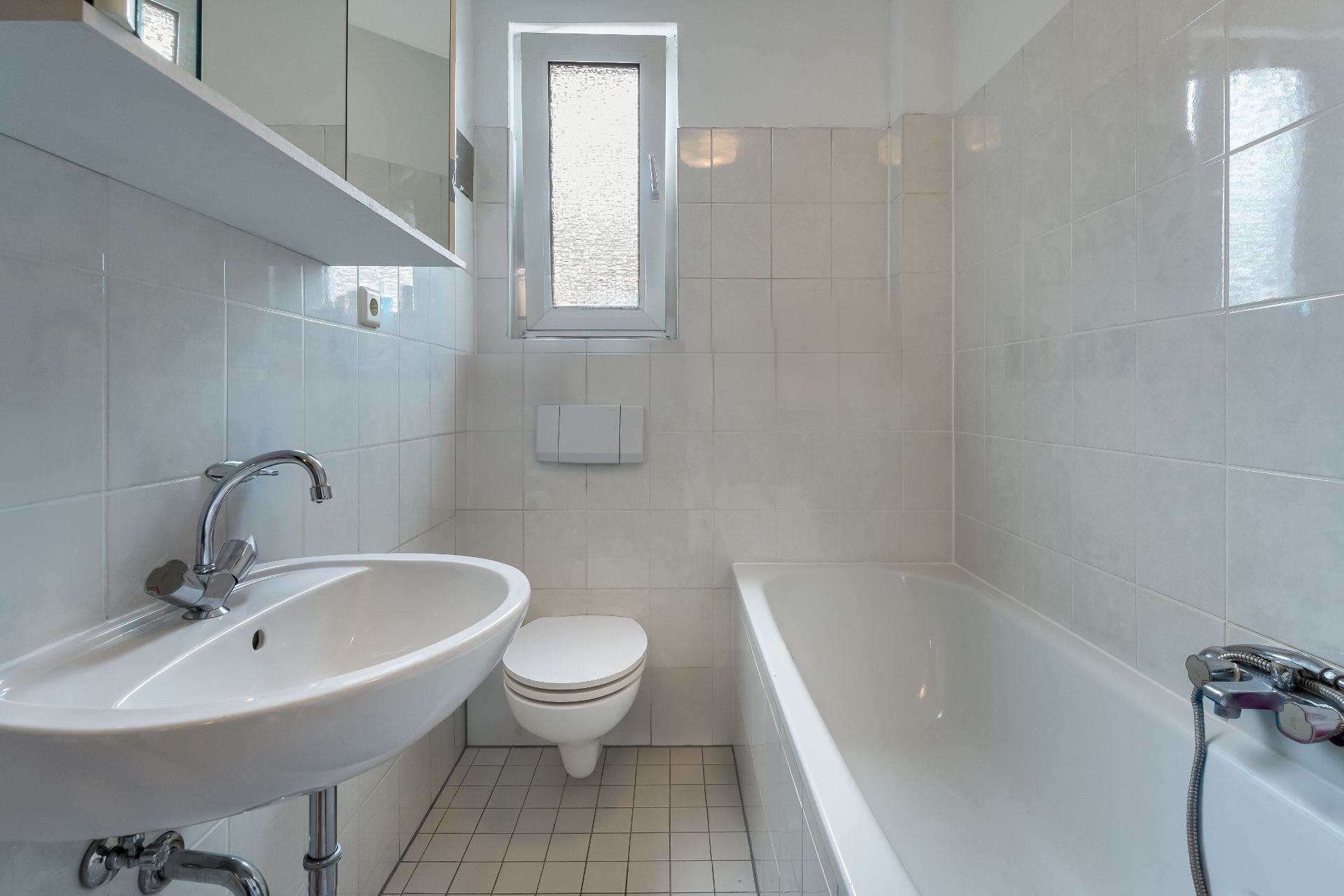 Helles Badezimmer mit Waschbecken, Toilette, Badewanne und kleinem Fenster.