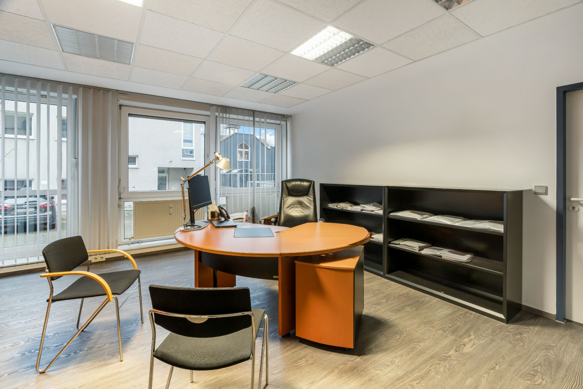 Modernes Büro mit großem Schreibtisch, zwei Stühlen und Regal mit Akten in einem hellen Raum.