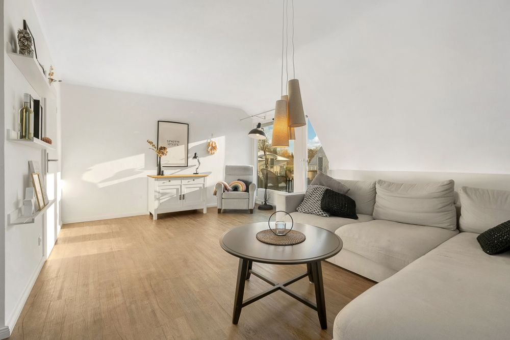 Modernes Wohnzimmer mit Ecksofa, Couchtisch, Hängelampen und Sessel vor großen Fenstern.