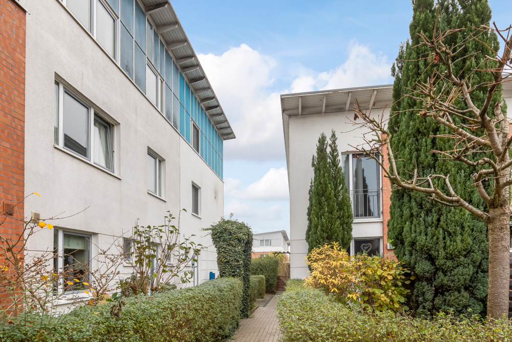 Ein Fußweg zwischen zwei modernen Wohngebäuden mit Büschen und Bäumen am Rand.