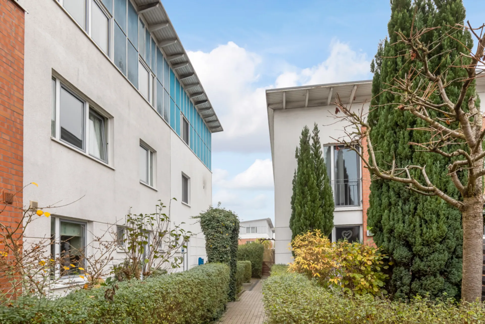 Ein Fußweg zwischen zwei modernen Wohngebäuden mit Büschen und Bäumen am Rand.